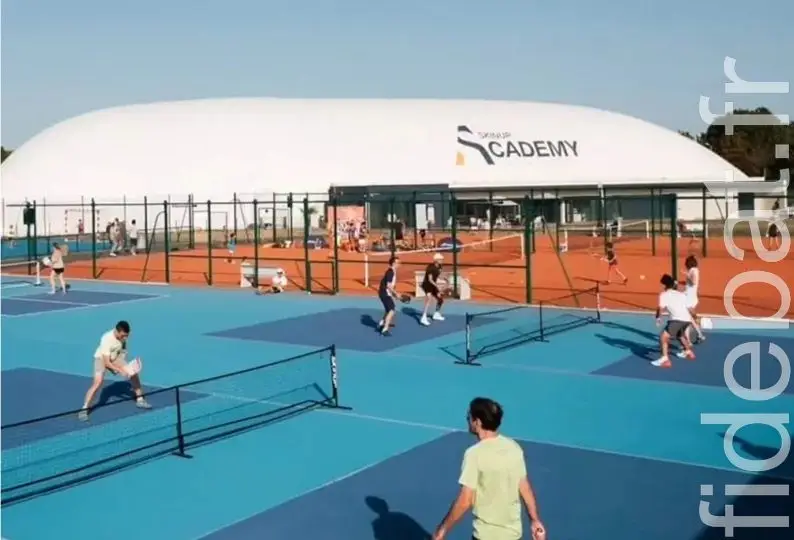 Joueurs sur courts de pickleball bleus en plein air devant une halle gonflable d'académie sportive