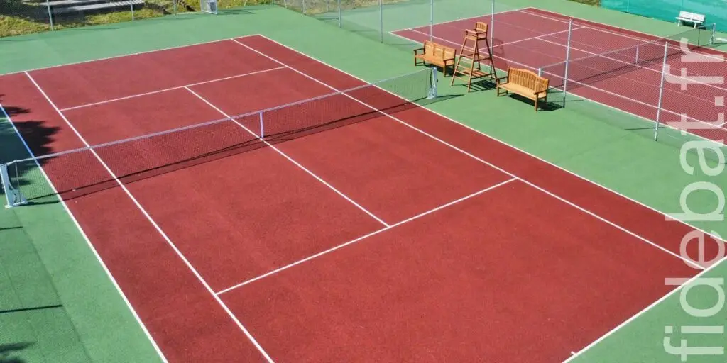 Terrain de tennis en gazon synthétique rouge avec filet et chaise d'arbitre, vue aérienne, installation SAE Tennis d'Aquitaine